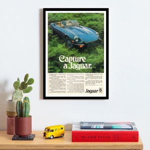 Puede incluir: Un anuncio impreso vintage para el automóvil deportivo Jaguar E-Type. El anuncio presenta un Jaguar E-Type azul conduciendo por un exuberante bosque verde. El texto dice "Capture a Jaguar".