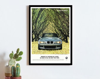 May include: A framed print of a vintage advertisement for a silver BMW car driving through a tunnel of trees. The text reads "Moments of freedom will never be given to you. You must take them."