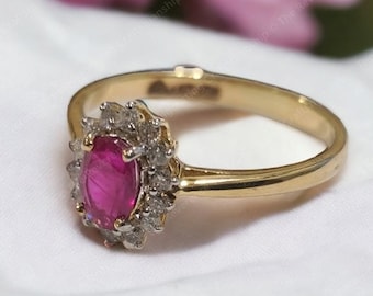 Pode incluir: Um anel de ouro com um grande rubi oval rodeado por diamantes menores. O anel está colocado sobre um fundo de tecido branco.