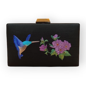 Impresionante clutch con un vibrante colibrí bordado en azul posado sobre flores intrincadamente tejidas, un toque de elegancia para cualquier outfit.