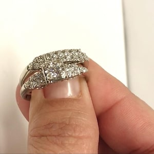 May include: A silver ring set with a large, square-cut diamond surrounded by smaller diamonds. The ring is worn on a finger.