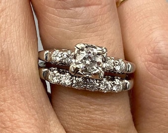 Könnte beinhalten: Ein Verlobungsring aus Weißgold mit einem runden Diamanten in der Mitte und einem Diamantenband. Der Ring befindet sich an einem Finger.