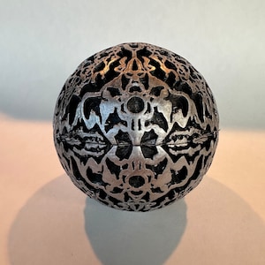 May include: A silver sphere with a detailed, intricate black design. The sphere has a smooth, metallic finish and a three-dimensional pattern.