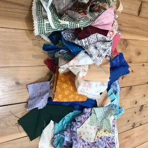 May include: A pile of colourful fabric scraps in various patterns and textures, including floral, plaid, and geometric designs. The scraps are arranged in a random order, creating a visually interesting composition.