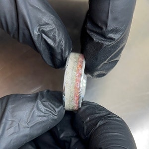 May include: A silver ring with a band of pink and white crushed stone inlay.