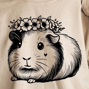 May include: A beige sweatshirt with a black and white illustration of a guinea pig wearing a flower crown. The guinea pig is looking at the viewer.
