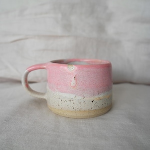 Può includere: Una piccola tazza in ceramica rosa e bianca con una glassa macchiettata. La tazza ha una forma arrotondata e un manico.