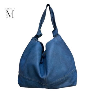 May include: A large, blue leather shoulder bag with a knotted handle. The bag has a rounded shape and a textured surface. The brand name "MAYMITH" is in the upper left corner.