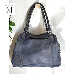 K&ouml;nnte beinhalten: Eine blaue Lederhandtasche mit zwei Henkeln und einem Rei&szlig;verschluss. Die Tasche hat eine strukturierte Oberfl&auml;che und Metallbeschl&auml;ge. Der Markenname "MAYMITH" ist oben links sichtbar.