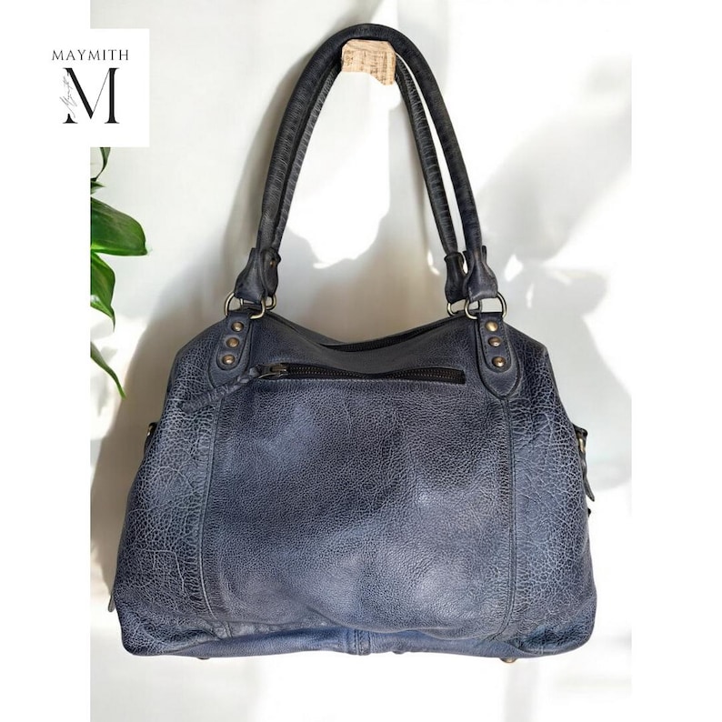 K&ouml;nnte beinhalten: Eine blaue Lederhandtasche mit zwei Henkeln und einem Rei&szlig;verschluss. Die Tasche hat eine strukturierte Oberfl&auml;che und Metallbeschl&auml;ge. Der Markenname "MAYMITH" ist oben links sichtbar.