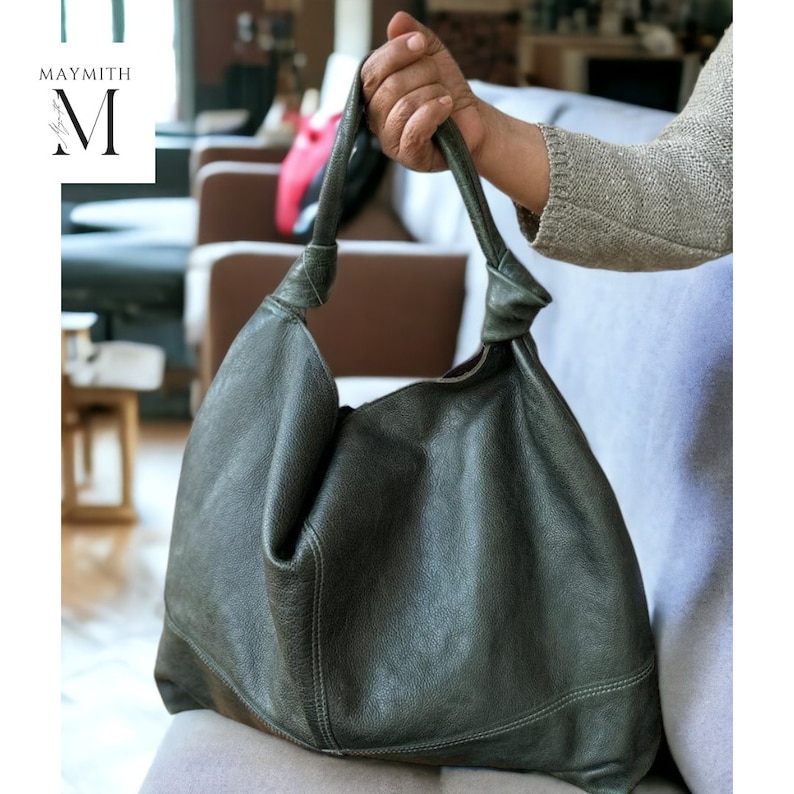May include: A dark green leather shoulder bag with a knotted handle. The bag has a slouchy design and visible stitching details. The bag is held by a person.