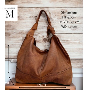 May include: A brown leather shoulder bag with a knotted strap. The bag is 16 inches high, 17 inches long, and 4 inches wide. The bag has a textured surface and is displayed against a wooden background. The brand name "MAYMITH" is in the upper left corner.