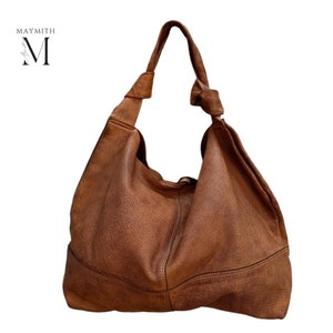 May include: A large, brown leather shoulder bag with a knotted strap. The bag has a slouchy design and a textured surface. The brand name "MAYMITH" is in the upper left corner.