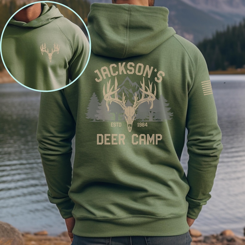 May include: Green hooded sweatshirt with a deer skull graphic on the back, featuring the text "Jackson's Deer Camp ESTD 1984." A smaller deer antler graphic is on the front. The sweatshirt is a solid green color.