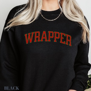May include: Black sweatshirt featuring the word "WRAPPER" in red with a green border. The word "BLACK" is printed at the bottom of the sweatshirt.