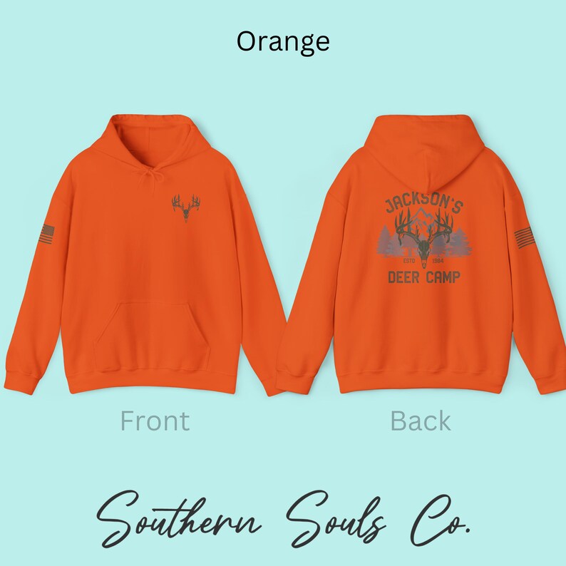May include: Orange hoodie with a front pocket and a hood. The front features a deer antler graphic. The back displays "Jackson's Deer Camp" text and a deer antler graphic. The sleeves have a small American flag design.