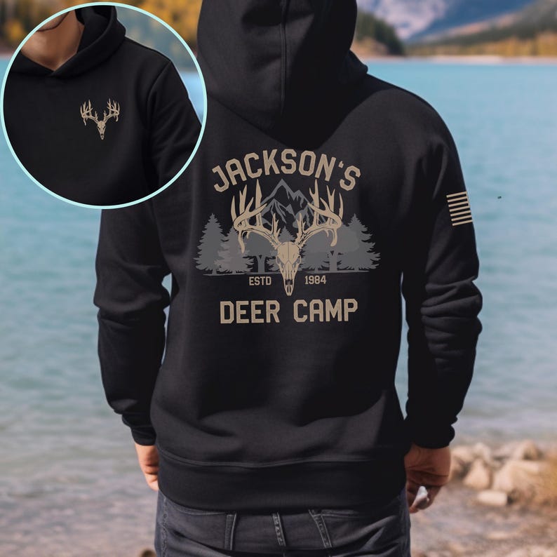 May include: Black hoodie with a deer antler graphic on the front and back. The back features the text "Jackson's Deer Camp" with a deer skull, mountain, and forest design. The hoodie also has a small American flag on the right sleeve.