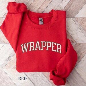 May include: Red sweatshirt with the word "WRAPPER" printed in white with a vintage style font.