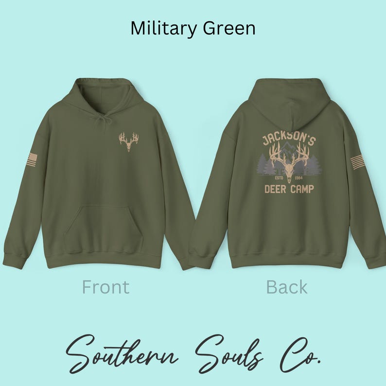 May include: Military green hoodie with a front pocket and a hood. The front features a deer antler graphic, and the back displays "Jackson's Deer Camp" with a deer antler graphic and the text "ESTD 1984". The sleeve has a small American flag.