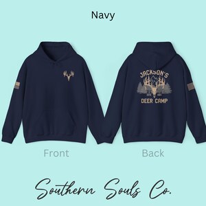 May include: Navy blue hoodie with a deer antler graphic on the front and back. The back of the hoodie features the text "Jackson's Deer Camp Estd 1964". The front of the hoodie has a small deer antler graphic. The text "Navy" is at the top.