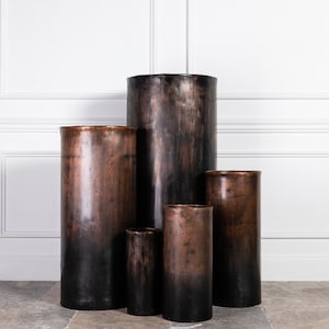 Peut inclure: Ensemble de cinq pots en cuivre de différentes tailles, avec une finition vieillie et patinée. Les pots sont disposés en forme de pyramide, le plus grand en bas et le plus petit en haut.
