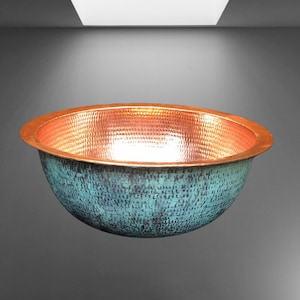 Op de afbeelding: Een gehamerde koperen gootsteen met een turquoise patina. De gootsteen is rond en heeft een licht uitlopende rand.
