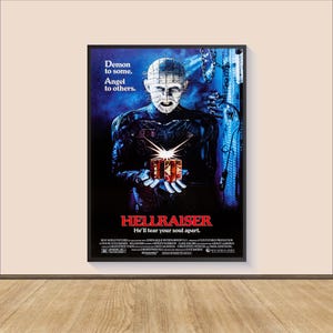 Puede incluir: Un póster enmarcado de la película "Hellraiser". El póster presenta una figura central con alfileres en la cabeza, sosteniendo una caja de rompecabezas. El texto incluye "Demon to some. Angel to others." y "He'll tear your soul apart."