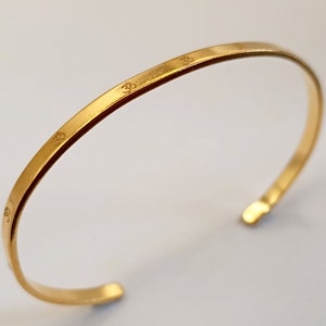 Puede incluir: Un brazalete dorado de diseño sencillo. El brazalete está grabado con el símbolo Om.