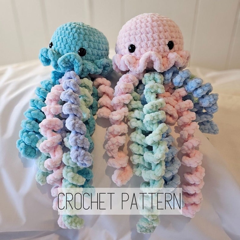 May include: Two crocheted jellyfish amigurumi toys, one in pink and one in blue, with long, curled tentacles. The tentacles are a gradient of pink, blue, and green. The text "CROCHET PATTERN" is visible at the bottom of the image.