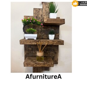 May include: A rustic, wooden wall shelf unit with three shelves. The shelves are made of reclaimed wood and hold small potted plants and a glass diffuser bottle. The text "AfurnitureA" is at the bottom.