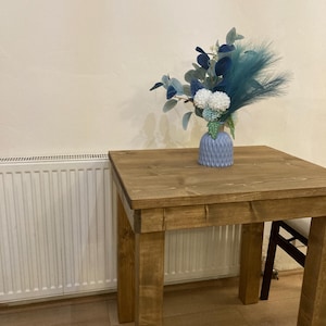 K&ouml;nnte beinhalten: Ein kleiner Holztisch mit hellbrauner Oberfl&auml;che. Ein blauer und wei&szlig;er Blumenstrau&szlig; steht in einer blauen Keramikvase auf dem Tisch.
