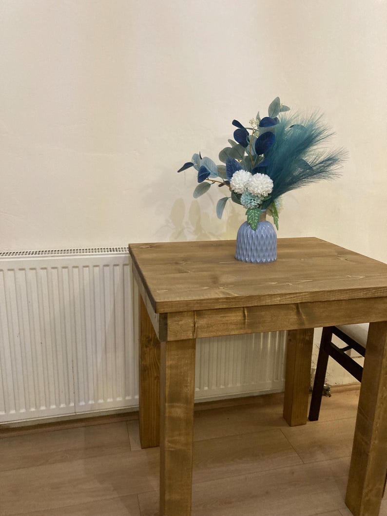 K&ouml;nnte beinhalten: Ein kleiner Holztisch mit hellbrauner Oberfl&auml;che. Ein blauer und wei&szlig;er Blumenstrau&szlig; steht in einer blauen Keramikvase auf dem Tisch.