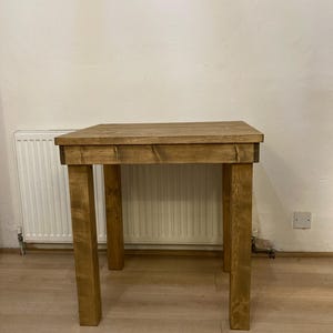 K&ouml;nnte beinhalten: Ein rustikaler Holztisch mit brauner Beize. Der Tisch hat eine rechteckige Tischplatte und vier Beine. Der Tisch steht auf einem hellen Holzboden.