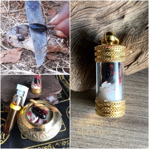 Puede incluir: Un colgante cilíndrico de cristal con tapas de metal dorado que contiene fragmentos blancos y negros con motas rojas. El conjunto incluye un pequeño cuenco de latón lleno de arroz blanco, partículas rojas y una piedra negra.
