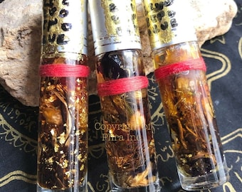 Puede incluir: Tres pequeñas botellas de vidrio llenas de un líquido dorado y varias hierbas y flores. Las botellas están coronadas con tapas plateadas y una cuerda roja. Las botellas están sobre una superficie oscura.