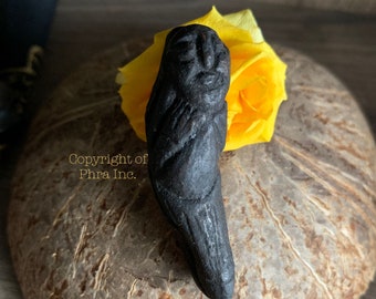 May include: A black carved wooden figurine of a person with a detailed face and body. The figurine is resting on a yellow flower and a brown surface.