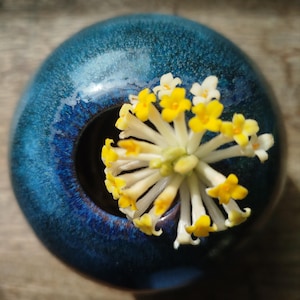 May include: A white ceramic mug with a black handle and the text "But First, Coffee" in a black, handwritten-style font. The mug is on a white surface.