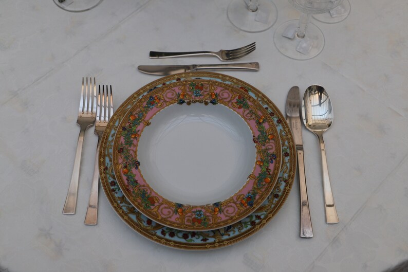 Puede incluir: Un plato de porcelana blanca con un patr&oacute;n floral colorido y detalles dorados. El plato est&aacute; puesto con un tenedor, un cuchillo y una cuchara.