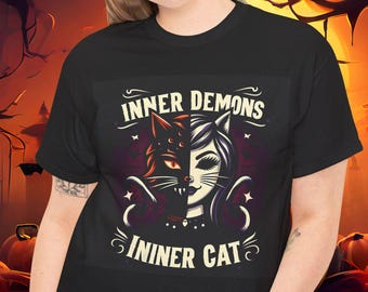 May include: Black t-shirt featuring a split design of a cat's face, half demonic and half angelic, with the text "INNER DEMONS" and "INNER CAT". The design is in shades of red, black, and white, with a Halloween theme.