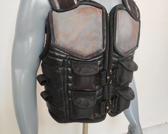 May include: A black tactical vest with multiple pockets and buckles. The vest has a gray padded chest panel with a zipper closure.