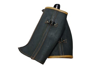 May include: A pair of black leather gaiters with brown leather trim and stitching. The gaiters have a strap and buckle at the top.