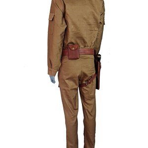 May include: A tan jumpsuit with a brown leather belt and a holster. The jumpsuit has a collared shirt with long sleeves and a zipper closure. The pants have a straight leg and a zipper fly.