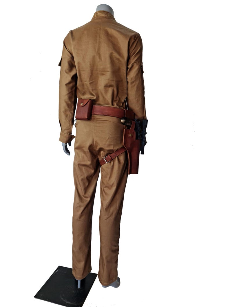 May include: A tan jumpsuit with a brown leather belt and a holster for a weapon. The jumpsuit has a collared shirt and long sleeves.