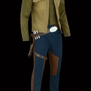 May include: A tan jacket with a blue and red stripe on the shoulder, worn over a blue shirt and dark blue trousers with brown leather accents. The trousers have a brown leather belt with a silver buckle.