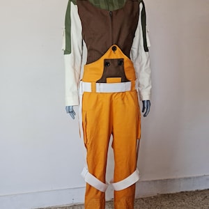 Puede incluir: Un disfraz de cuerpo entero con una combinación de colores verde, marrón, blanco y naranja. La parte superior tiene un cuello verde, un pecho marrón y mangas blancas. Los pantalones naranjas tienen detalles blancos y un cinturón blanco.