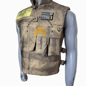 Könnte beinhalten: Eine beige taktische Weste mit mehreren Taschen, Riemen und Schnallen. Die Weste hat einen hohen Kragen und einen gelben Aufnäher auf der Schulter. Ein schwarzer Aufnäher mit einem kreisförmigen Design und zwei gelben Punkten befindet sich auf der Brust. Die Weste ist zum Überziehen von Kleidung konzipiert.