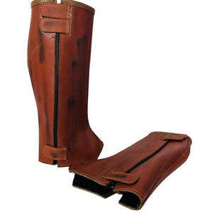Op de afbeelding: Een paar bruine leren rijlaarzen gaiters met een rits aan de achterkant. De gaiters hebben een verweerde look en zijn gemaakt van zacht, soepel leer.