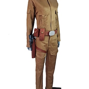May include: A tan jumpsuit with a collared shirt, a brown leather belt with a silver buckle, and a brown leather holster with a black gun. The jumpsuit has two large pockets on the front and two smaller pockets on the chest.