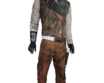 May include: A brown leather vest with a gray and brown patterned shirt, brown pants with a cargo pocket, and a brown belt with a silver buckle. The vest has a brown leather strap and a black and silver holster.
