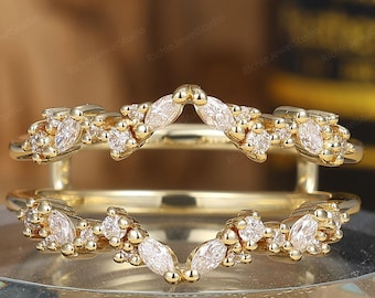 May include: A gold ring guard featuring two bands connected by vertical bars. Each band is adorned with a series of marquise and round-cut clear stones arranged in a chevron pattern, creating a symmetrical design that frames a center stone.